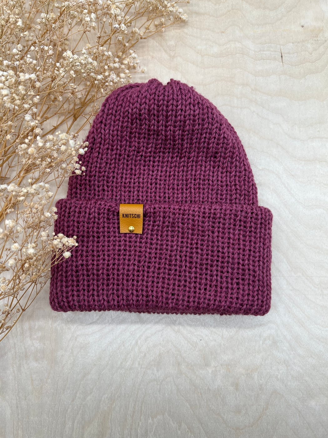 Genuine KNITSCHI beanie in a berry shade with faux leather label