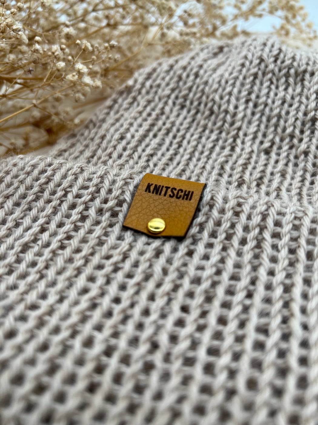 Close-up of the stitches and the KNITSCHI label on a natural-colored beanie