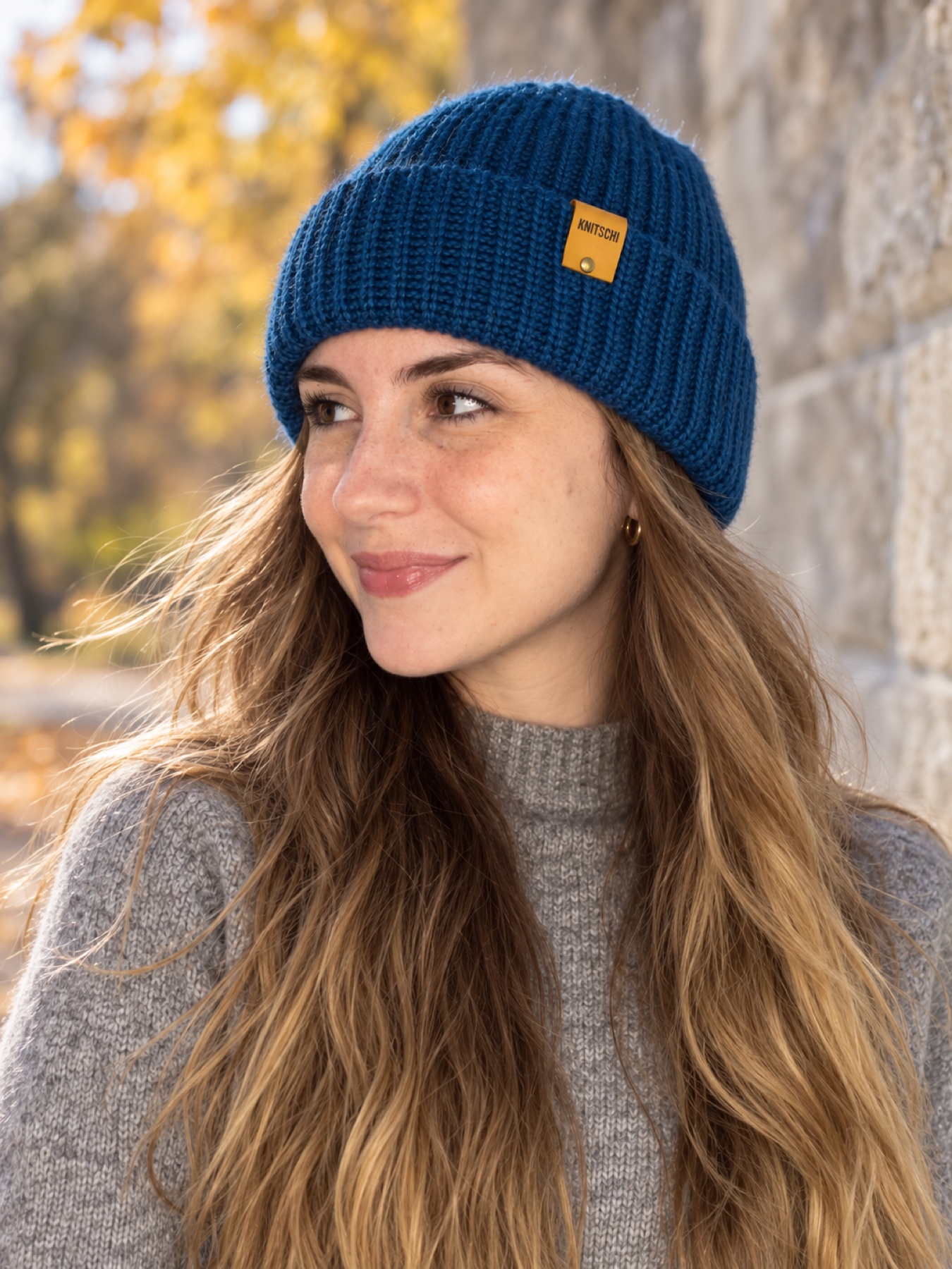 Close-up of the KNITSCHI hat on the model in front of a natural stone wall