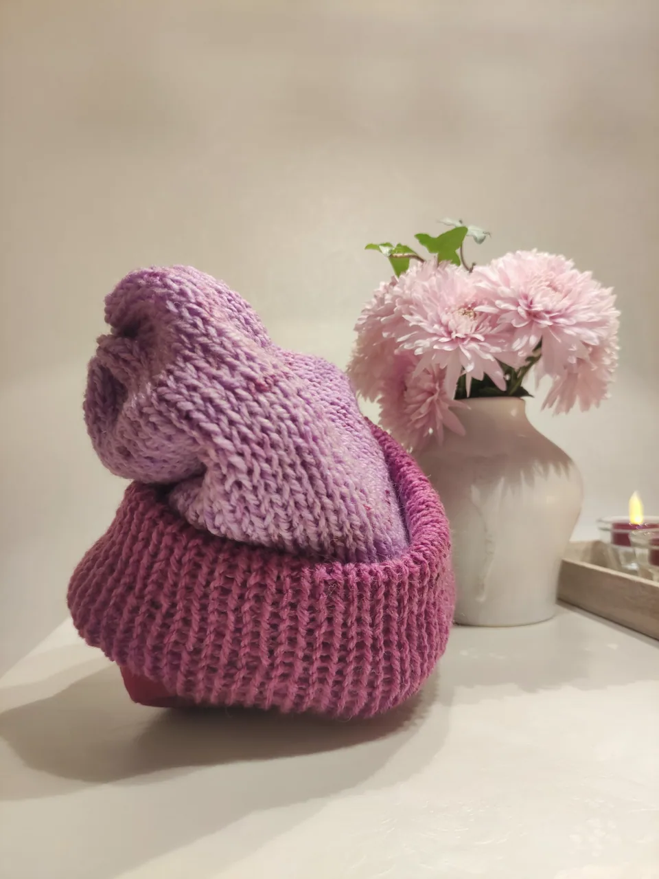 Zwei frühe KNITSCHI-Mützen in Rosatönen neben einer Blumenvase
