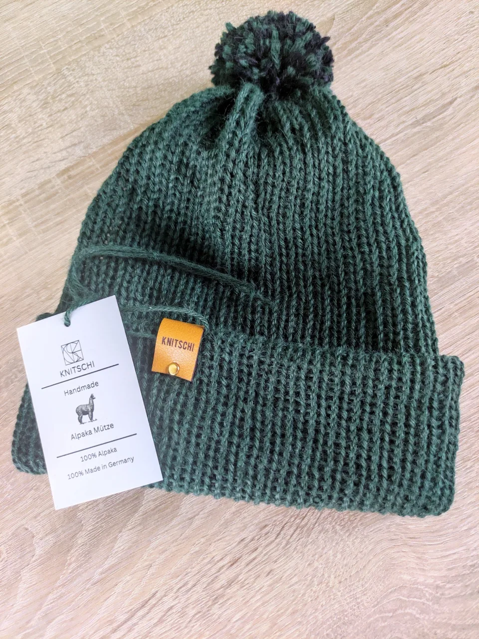 Fertige grüne KNITSCHI-Mütze mit Produktanhänger und Markenlabel