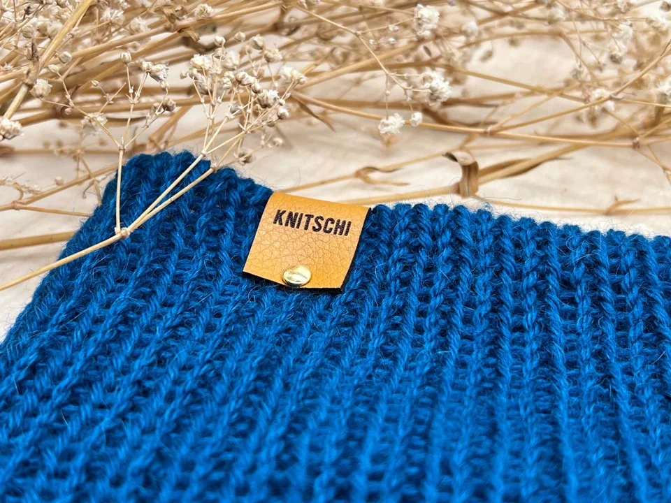 Nahaufnahme eines KNITSCHI-Kunstleder-Labels auf blauem Strick