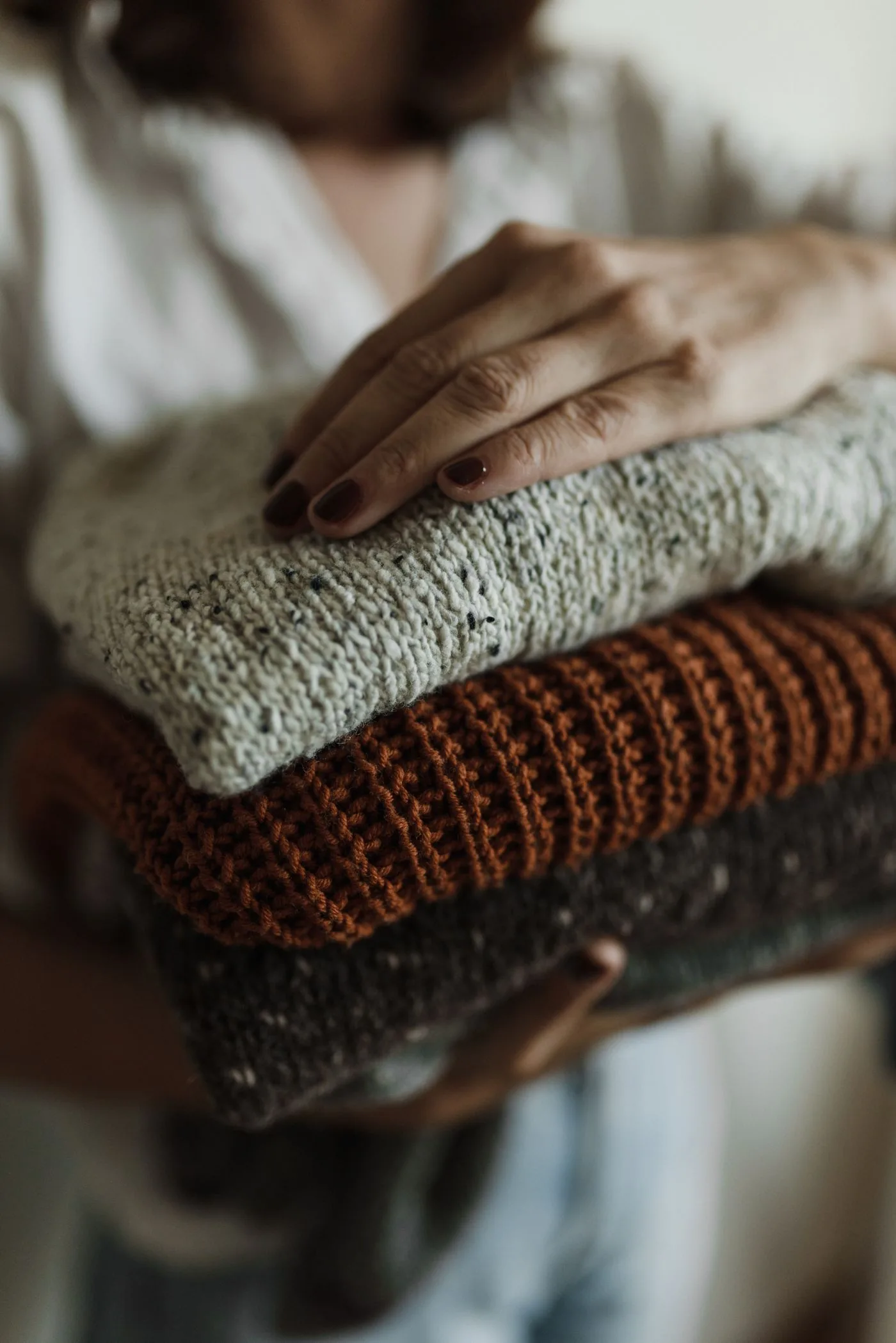 Eine Hand ruht auf einem Stapel gefalteter Stricktextilien